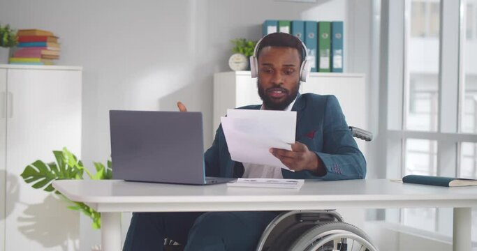Disabled young man in wheelchair working in office having video call on laptop