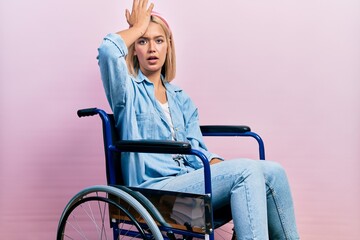 Beautiful blonde woman sitting on wheelchair surprised with hand on head for mistake, remember...