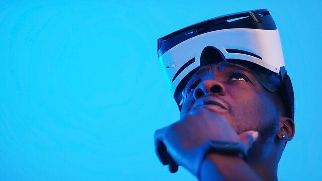 Pensive African-American guy with virtual reality glasses on his forehead looking around. High quality photo