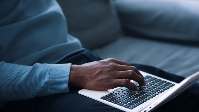 Closeup view of hands of a guy using a laptop placed on his lap and holding phone . High quality photo