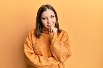 Young beautiful woman wearing turtleneck sweater smiling looking confident at the camera with crossed arms and hand on chin. thinking positive.