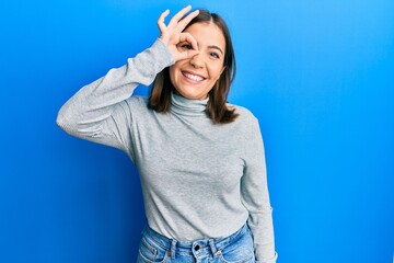 Young beautiful woman wearing casual turtleneck sweater smiling happy doing ok sign with hand on eye looking through fingers