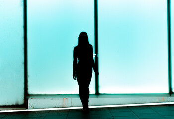 Silueta femenina sensual frente a un panel luminoso de color azul