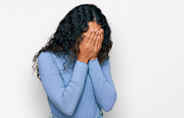 Young hispanic woman with curly hair wearing casual clothes with sad expression covering face with hands while crying. depression concept.