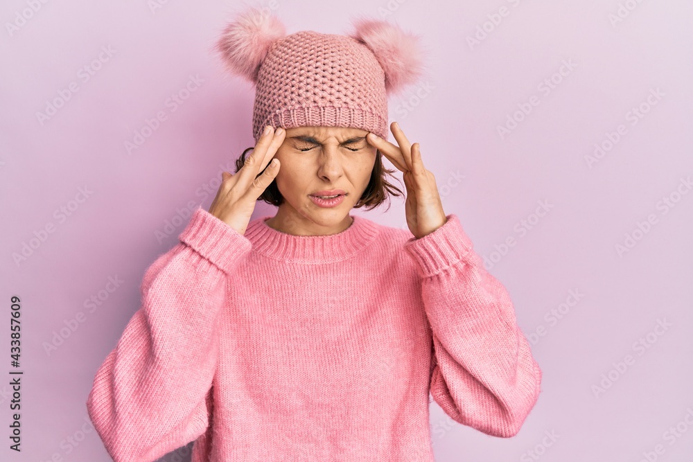 Poster young brunette woman wearing cute wool cap with hand on head for pain in head because stress. suffer