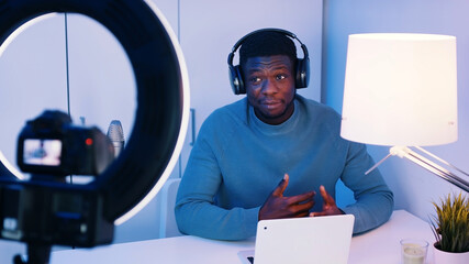 African American man wearing headphones sitting at the table explaining something. Concept of online classes or podcasts. Recording at the studio. High quality photo