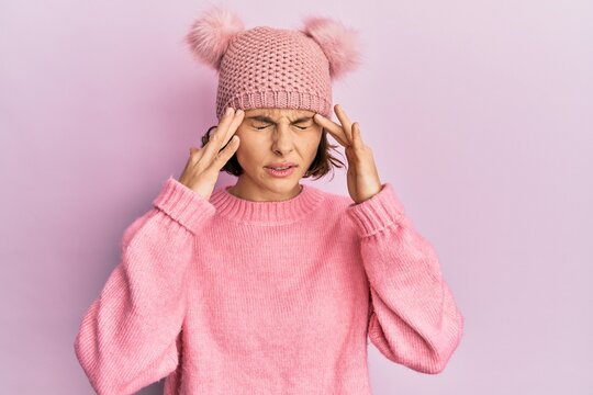 Young brunette woman wearing cute wool cap with hand on head for pain in head because stress. suffering migraine.
