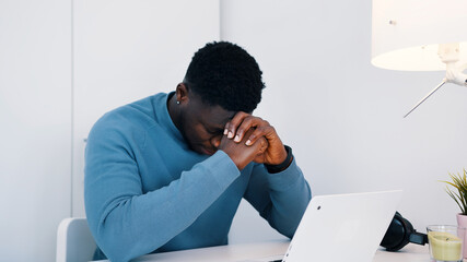 African American black man sitting at the table in front of a laptop working. Stressed out man working on his laptop. High quality photo