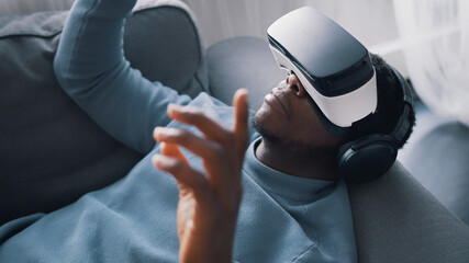 African-American man wearing virtual reality glasses and headset lying on the sofa. High quality photo