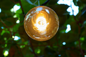 Macro closeup of a filament lamp in warm tone. Yellow lamp in a garden.
