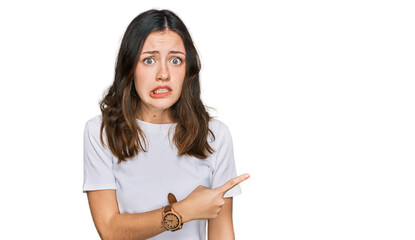 Young beautiful woman wearing casual white t shirt pointing aside worried and nervous with forefinger, concerned and surprised expression