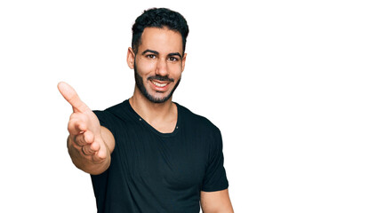 Hispanic man with beard wearing casual black t shirt smiling friendly offering handshake as greeting and welcoming. successful business.