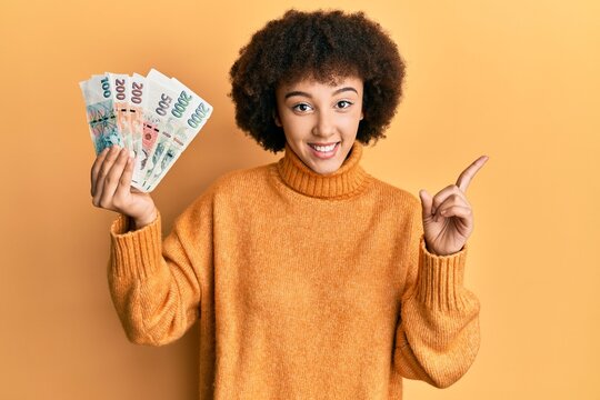 Young hispanic girl holding czech koruna banknotes smiling happy pointing with hand and finger to the side