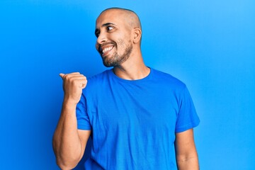 Hispanic adult man wearing casual blue t shirt pointing thumb up to the side smiling happy with open mouth