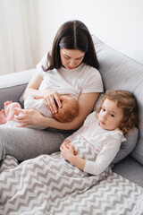 Breast feeding mama at home. Baby breastfeed on mothers hands, Cuddle a baby and talking to son, sad sister on the sofa watching 