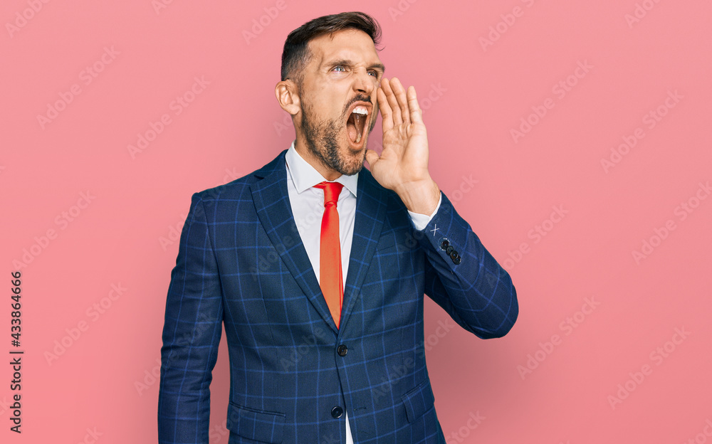 Poster handsome man with beard wearing business suit and tie shouting and screaming loud to side with hand 