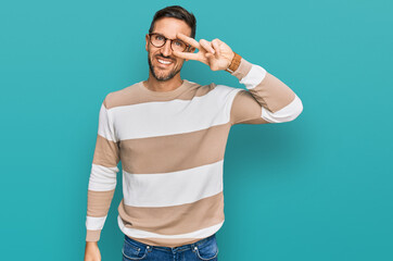 Handsome man with beard wearing casual clothes and glasses doing peace symbol with fingers over...