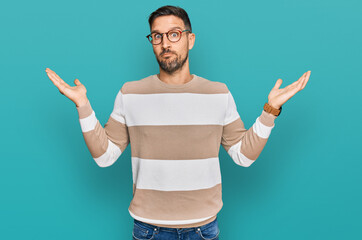 Handsome man with beard wearing casual clothes and glasses clueless and confused expression with...