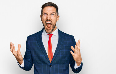 Handsome man with beard wearing business suit and tie crazy and mad shouting and yelling with aggressive expression and arms raised. frustration concept.