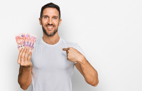 Handsome man with beard holding south african 50 rand banknotes pointing finger to one self smiling happy and proud
