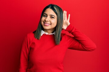 Young latin woman wearing casual clothes smiling with hand over ear listening an hearing to rumor or gossip. deafness concept.