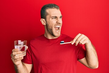 Young caucasian man holding toothbrush with toothpaste angry and mad screaming frustrated and...