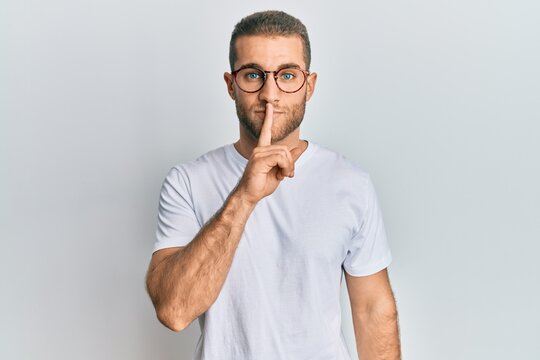 Young caucasian man wearing casual clothes and glasses asking to be quiet with finger on lips. silence and secret concept.