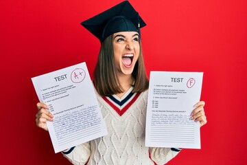 Young brunette girl wearing graduation cap showing exams angry and mad screaming frustrated and furious, shouting with anger looking up.