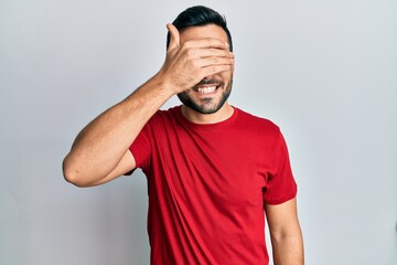 Young hispanic man wearing casual clothes smiling and laughing with hand on face covering eyes for surprise. blind concept.