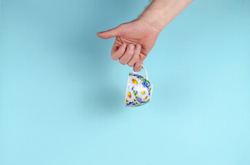 Hand and cup on blue background. Man holding White cup with painted flowers.