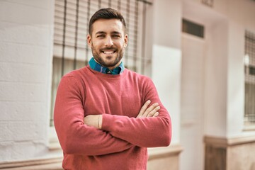 Young hispanic man with arms crossed smiling happy standing at the city.