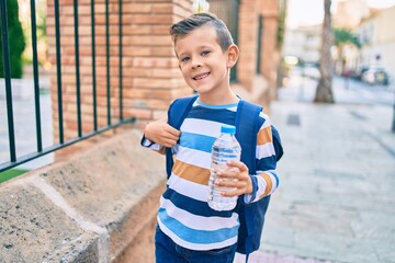 Adorable caucasian student boy smiling happy holding bottle of water standing at the city.