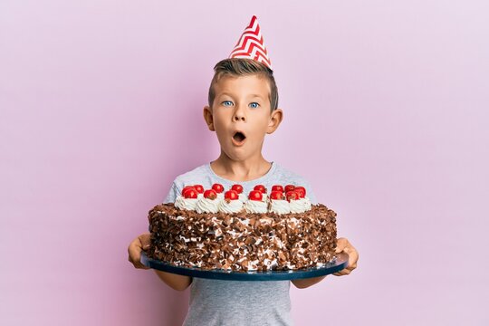 Adorable caucasian kid celebrating birthday with cake afraid and shocked with surprise and amazed expression, fear and excited face.