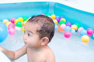 Fototapeta na wymiar Cute little boy 17 month with water and plastic ball toy in plastic pool. happy family in summer hollidays concept.