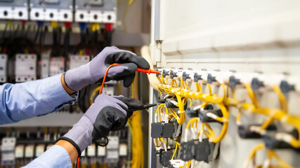 Electrical engineer using digital multi-meter measuring equipment to checking electric current voltage at circuit breaker and cable wiring system in main power distribution board.