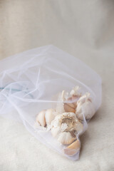 Close-up of garlic on a white tablecloth in a reusable eco bag. Home plant growing, cooking and spices. Sunlight and trending hard shadows. Conscious consumption. High quality photo
