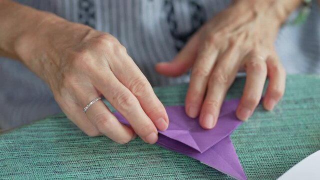 close up view of senior retired woman folding paper to make bird origami as a hobby at home