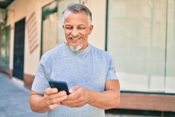 Middle age hispanic grey-haired man smiling happy using smartphone at the city.