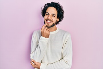 Handsome hispanic man wearing casual white sweater looking confident at the camera smiling with crossed arms and hand raised on chin. thinking positive.