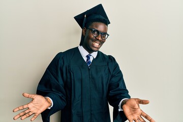 Handsome black man wearing graduation cap and ceremony robe smiling cheerful offering hands giving...