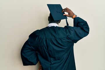 Handsome black man wearing graduation cap and ceremony robe backwards thinking about doubt with...