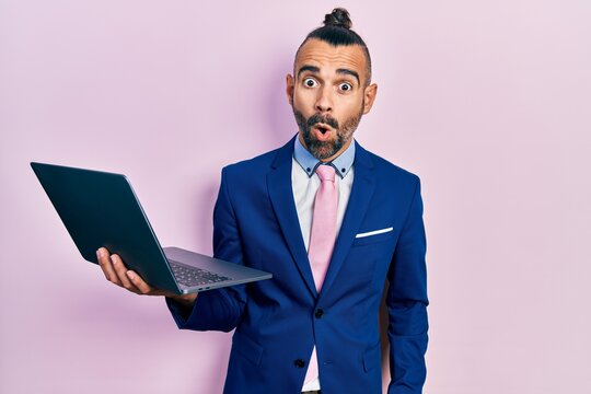 Young hispanic man working using computer laptop scared and amazed with open mouth for surprise, disbelief face