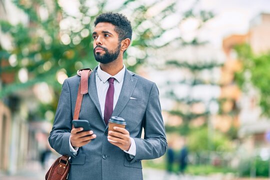 Young african american businessman with serious expression using smartphone and drinking coffee at the city.