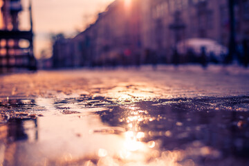 Streets in the late autumn, sidewalk illuminated sun. Close up view from the level of the puddle on the sidewalk