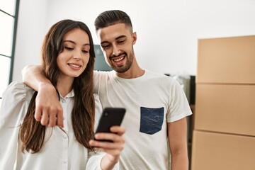 Young hispanic couple smiling happy using smartphone at new home.