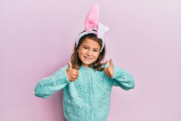 Little beautiful girl wearing cute easter bunny ears success sign doing positive gesture with hand,...