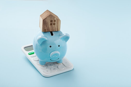House on piggy bank and calculator on blue background