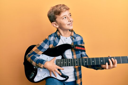 Little caucasian boy kid playing electric guitar smiling looking to the side and staring away thinking.