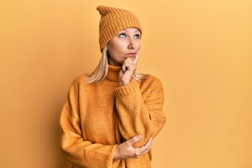 Middle age caucasian woman wearing wool winter sweater and hat serious face thinking about question with hand on chin, thoughtful about confusing idea