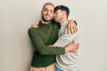 Homosexual gay couple standing together wearing casual clothes hugging oneself happy and positive,...